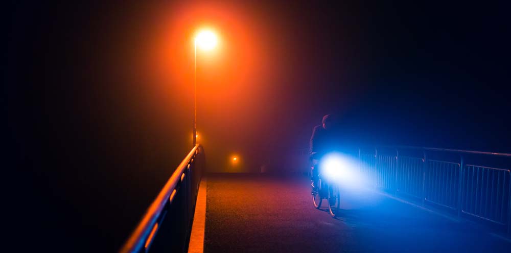 Person riding a bike on a dark bridge with a bright front bike light