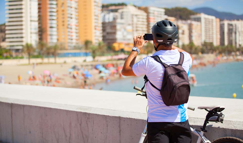 Man on a bike stopping to take a photo of a beach scene