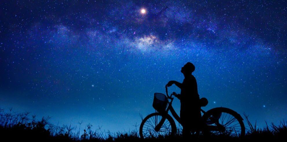 Silhouette of a person and a bike gazing at a star at night