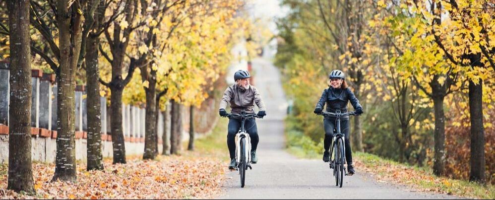 Two people with helmets riding ebikes side by side on a trail with falling leaves