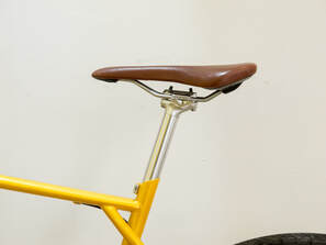 Yellow bike with a brown bicycle saddle