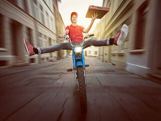 Man on a bike with legs out holding a pizza boxicture