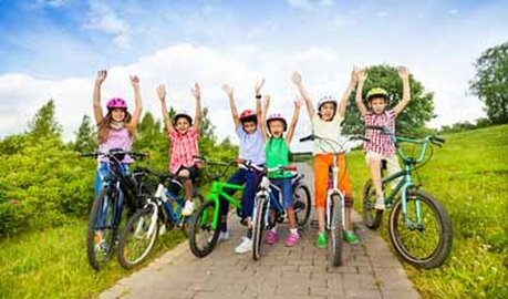 Row of children on bikes stopped on a trail with hands in the air