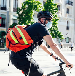Man riding a bike in a city wearing a bright messenger bag across one shoulder