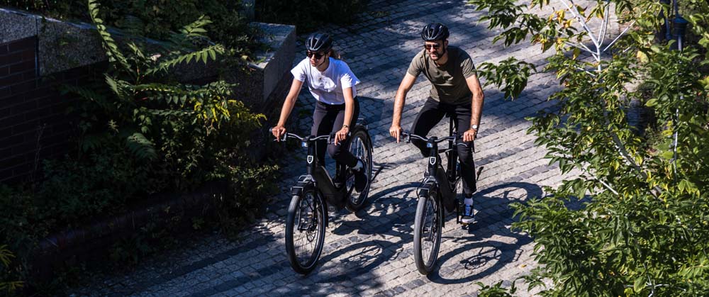 Two riders wearing helmets on Serial 1 ebikes on a wooded bike path