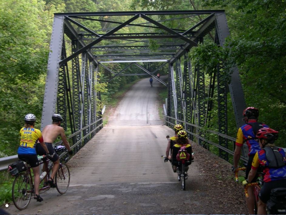 Group of cyclists on tandem bikes going over a bridge in a wooded area