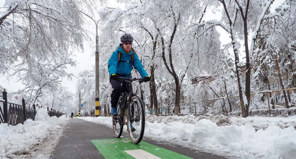 Cyclist biking on a city path in winter with snow