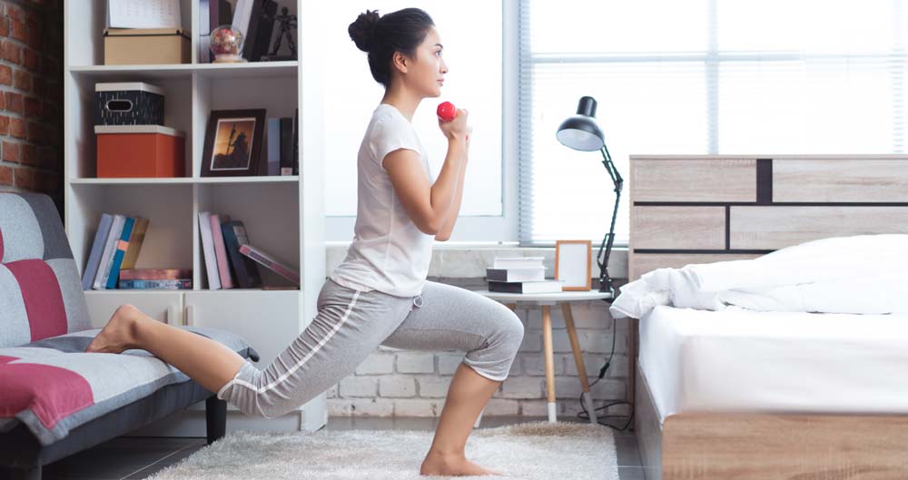 Woman doing a split squat and holding a weight in a bedroom